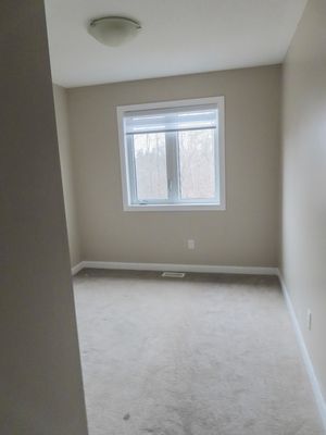 Vacant bedroom with beige carpet, neutral walls, and single window overlooking wooded area.