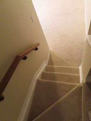 Carpeted staircase with wooden handrail leading upstairs, featuring white walls and baseboards in a residential home.
