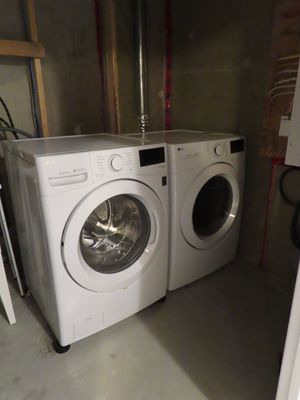 White LG front-load washer and dryer set installed side by side in a basement laundry area.