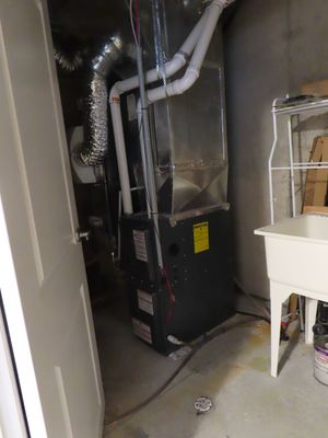 Residential gas furnace with flexible ductwork and PVC flue pipe installed in a utility room.