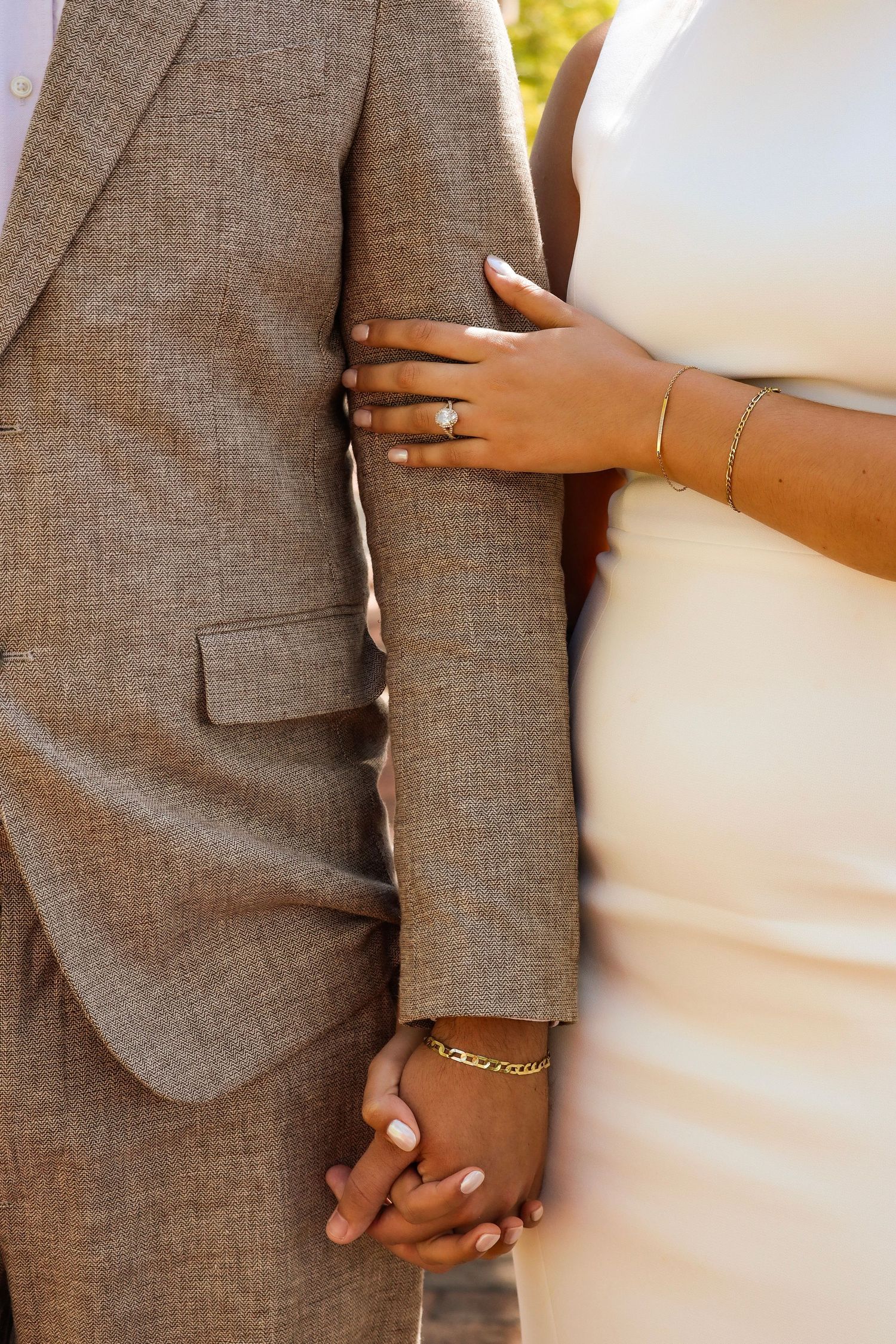Close-up of newlyweds holding hands, showing wedding rings against grey suit and white dress.