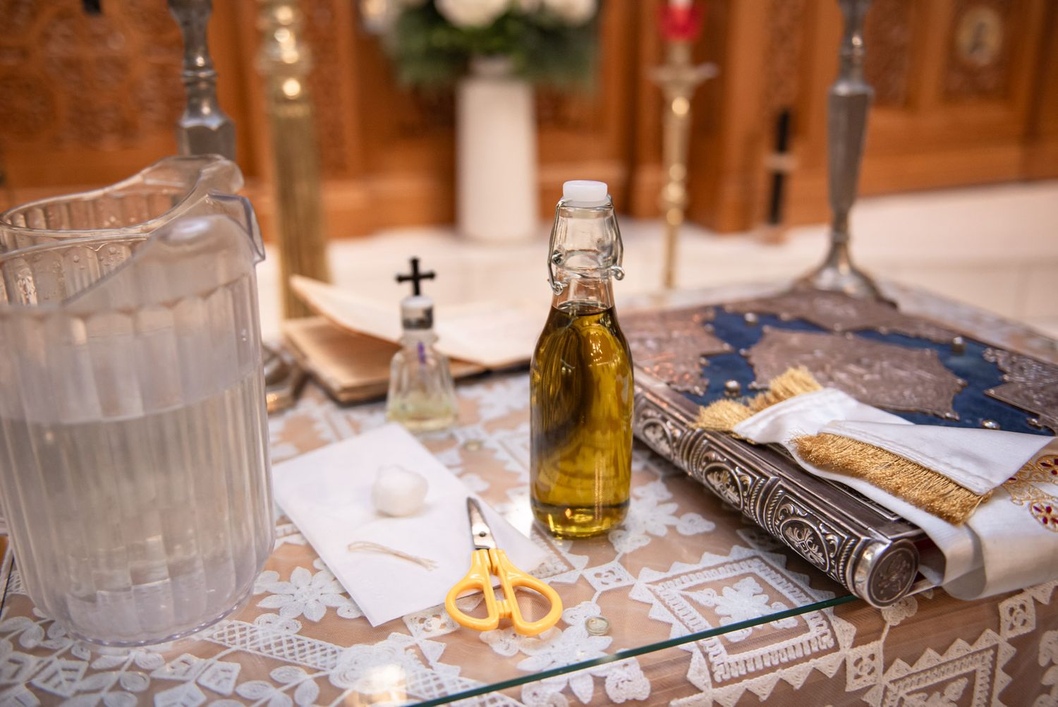 Orthodox baptism ceremony items including olive oil bottle, scissors, and ritual cloth on altar table.