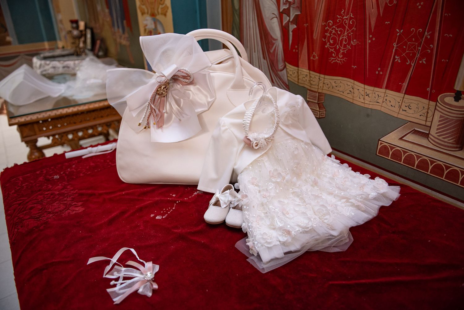 White baptism accessories including handbag, lace garment, and ribbon on red velvet surface.