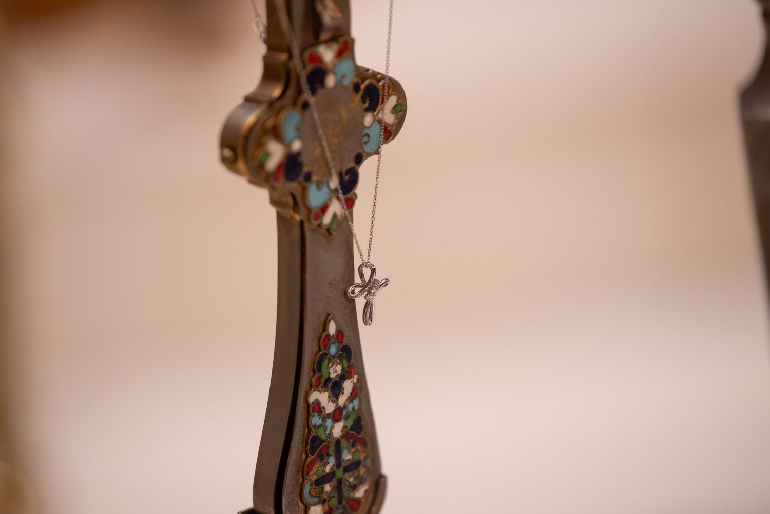 Ornate decorative cross with cross pendant necklace hanging against soft blurred background.
