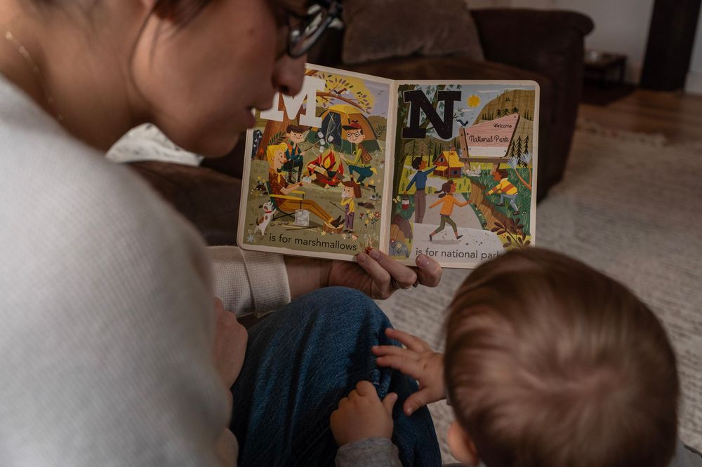 Adult and toddler reading a colorful illustrated alphabet book together on the floor at home.