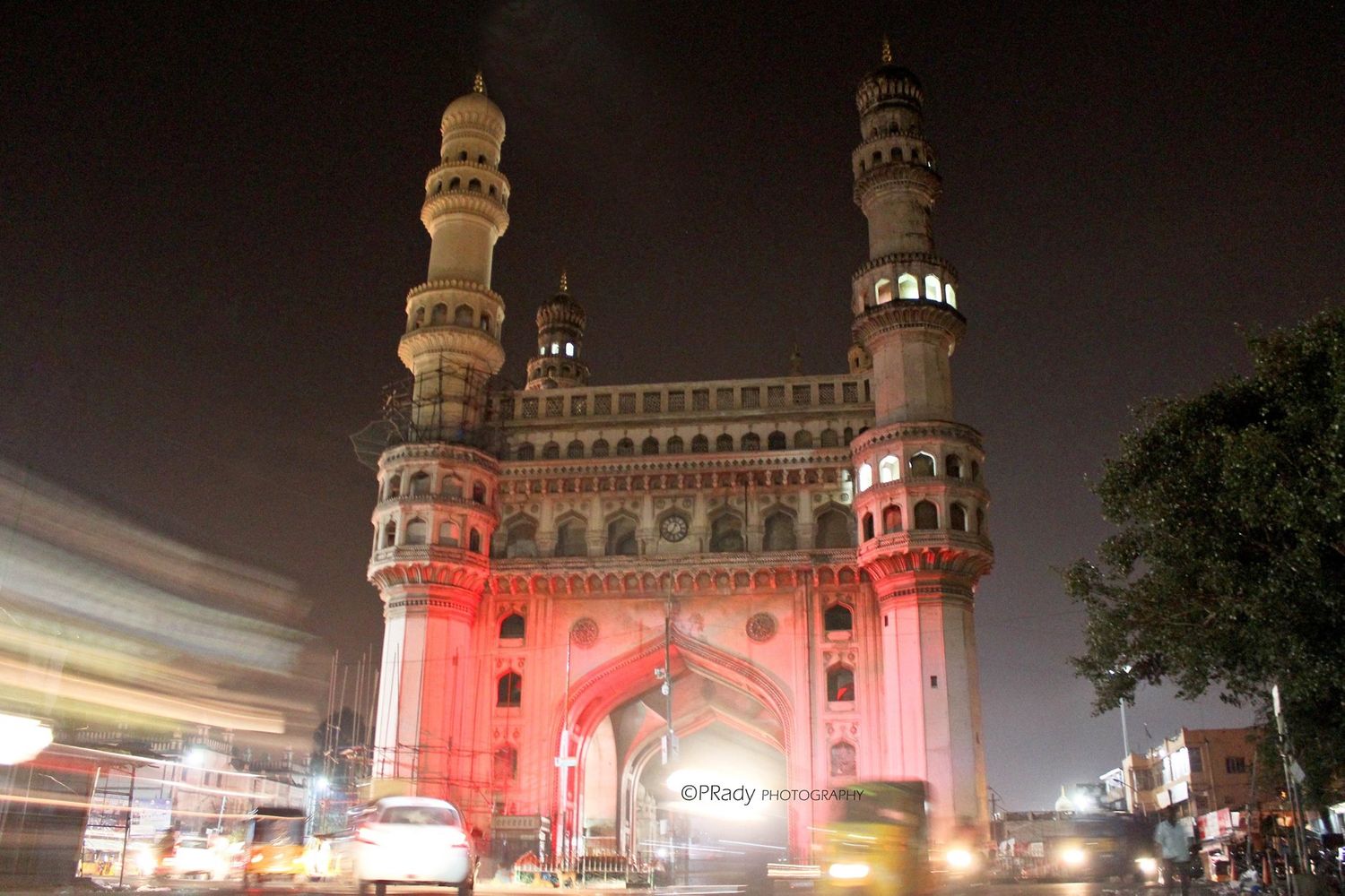 Illuminated Charminar monument in Hyderabad glows pink against the night sky, with its iconic four minarets.