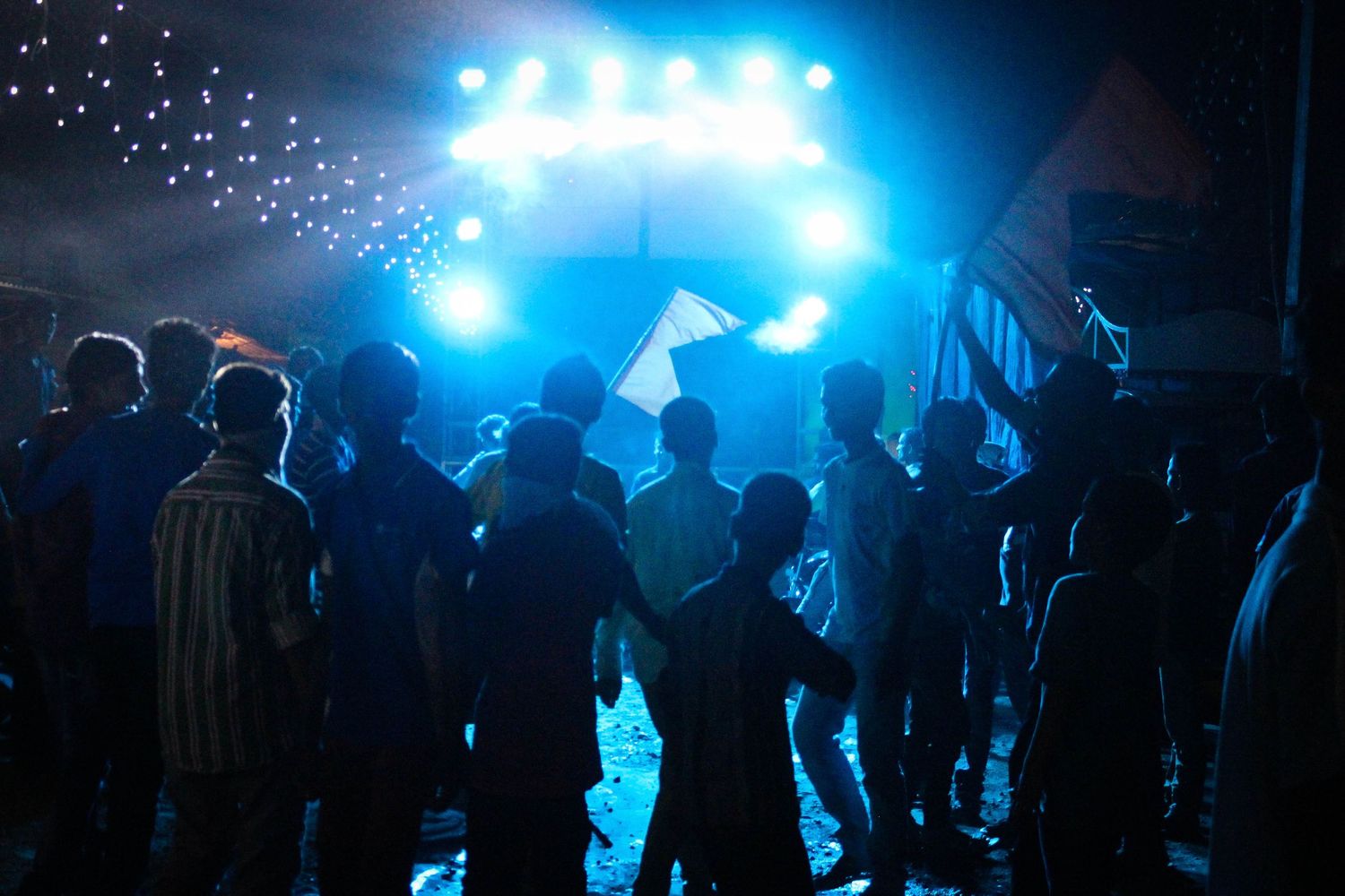 Silhouettes of concert crowd against bright blue stage lighting and special effects.