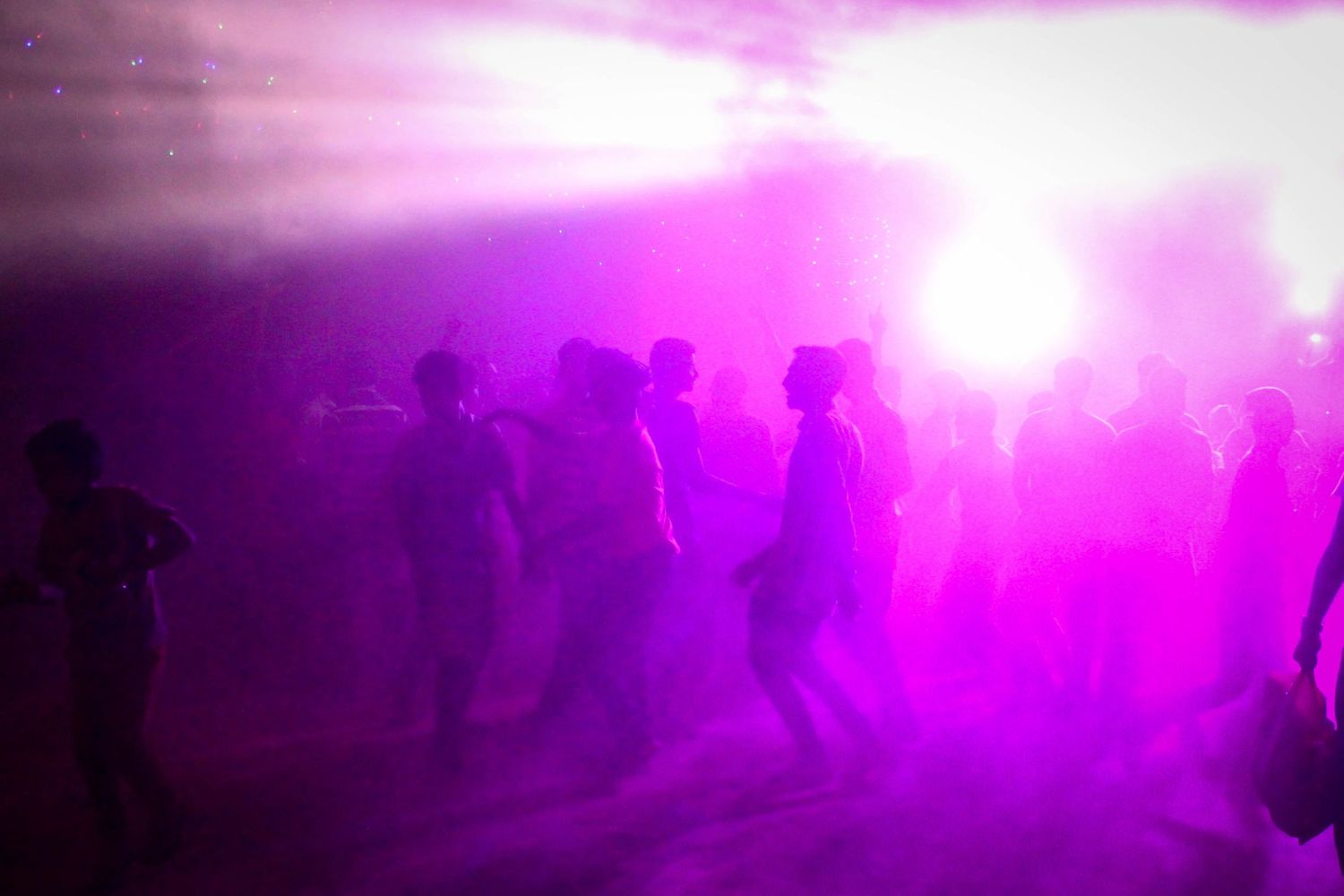 Dance floor scene bathed in vibrant pink lighting with people dancing in a misty atmosphere.