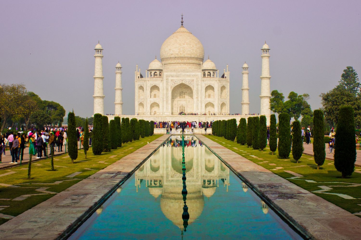 The iconic Taj Mahal and its reflection in a long pool surrounded by manicured gardens and visitors.