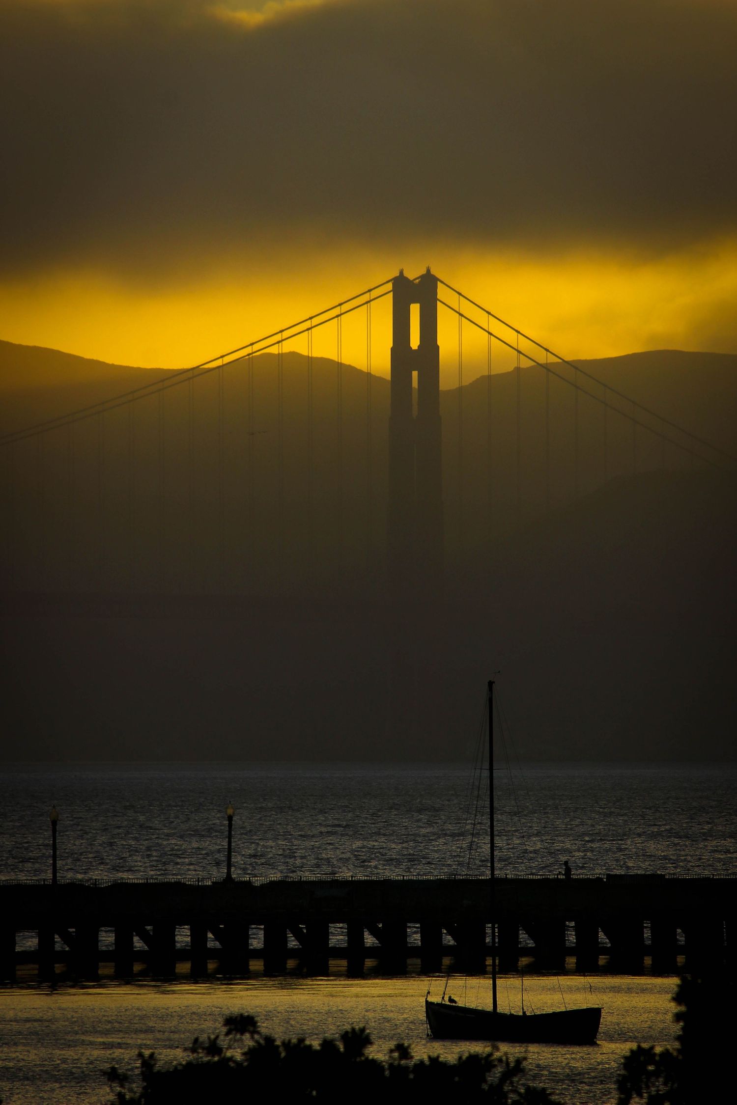 Silhouette of Golden Gate Bridge tower against dramatic golden sunset sky over San Francisco Bay.