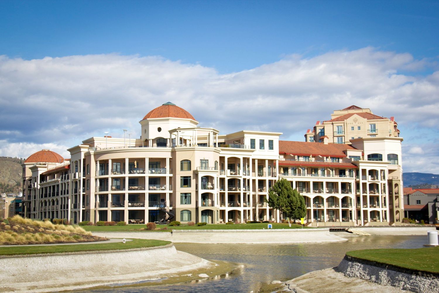 Luxurious waterfront resort building with Mediterranean architecture and reflecting pool.