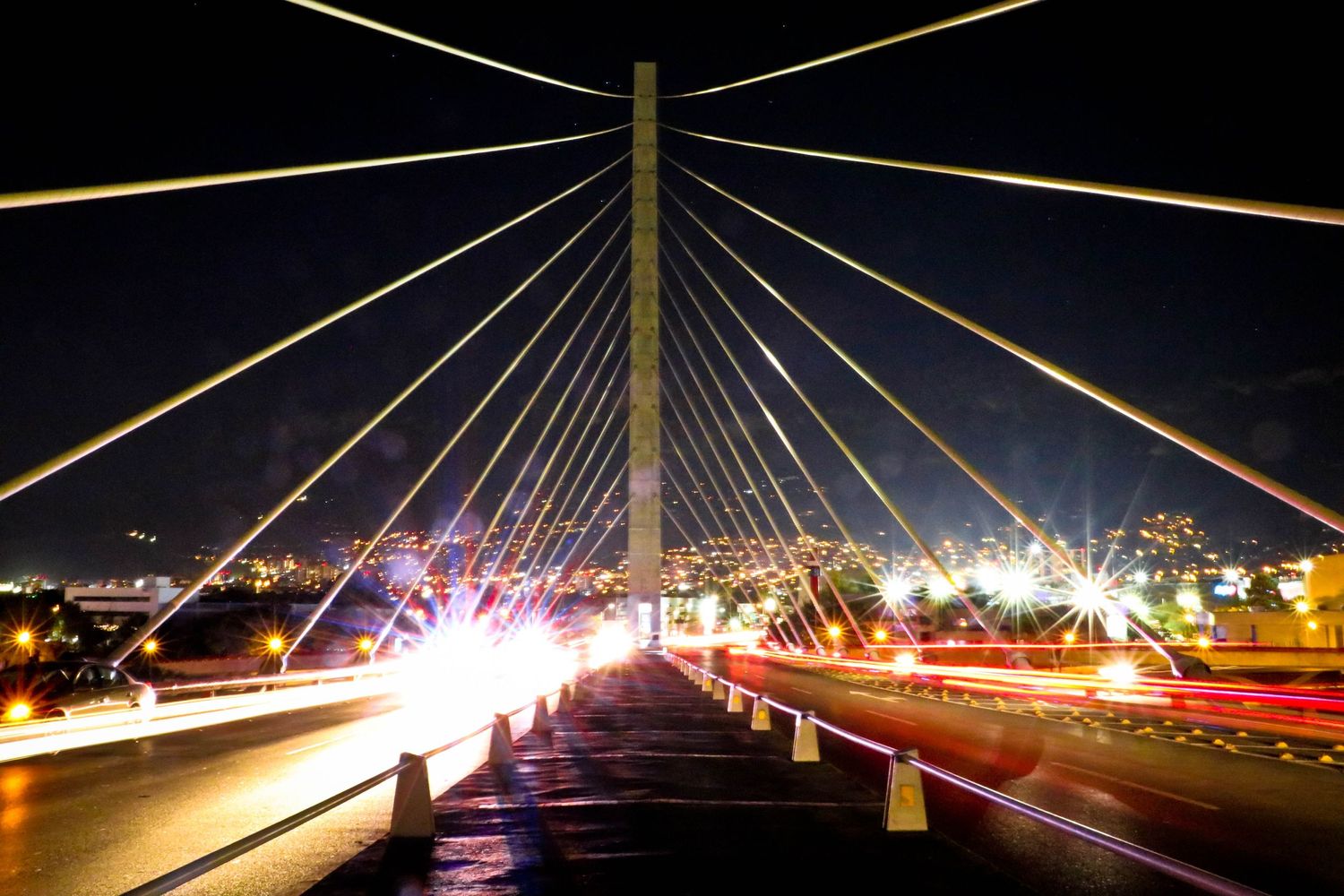 Modern cable-stayed bridge illuminated at night with light trails from traffic.