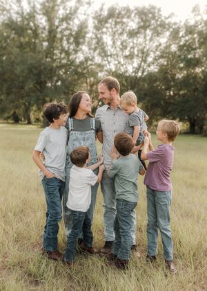 A happy family of six poses together in a green field, with parents and four children dressed in casual denim outfits.