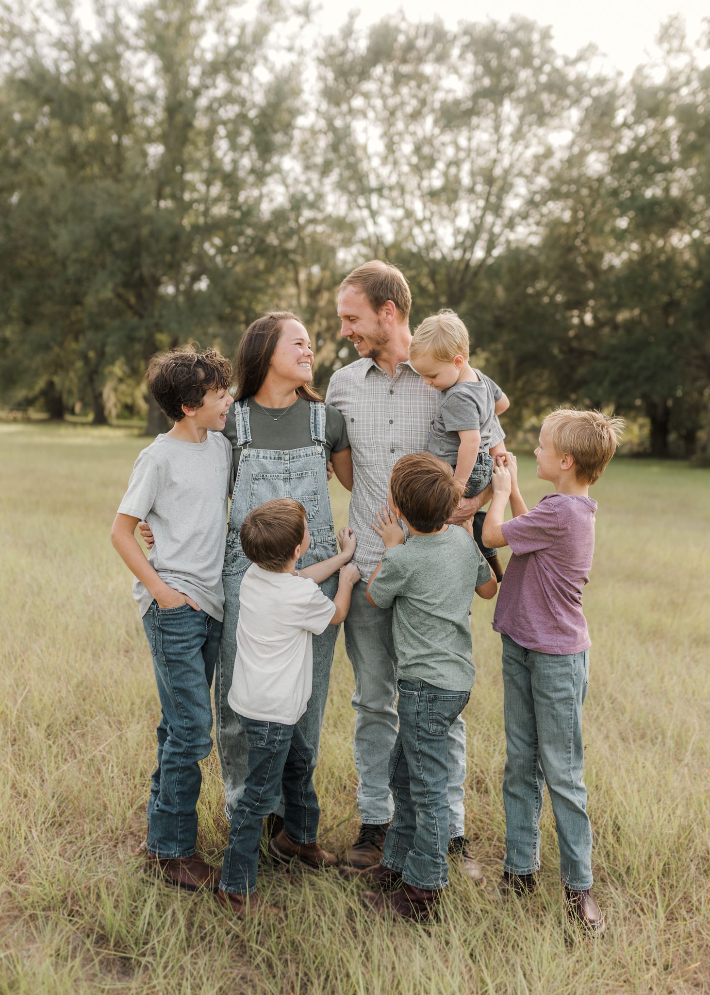 A happy family of six poses together in a green field, with parents and four children dressed in casual denim outfits.