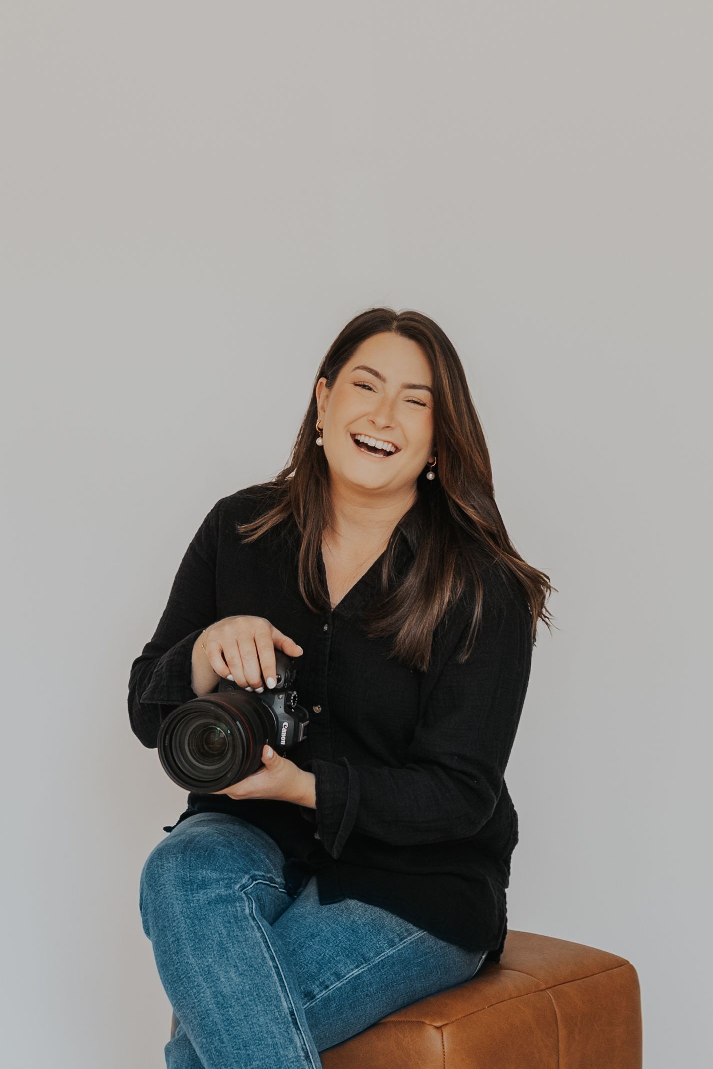 Professional photographer in white shirt and blue bandana poses with camera against grey background.