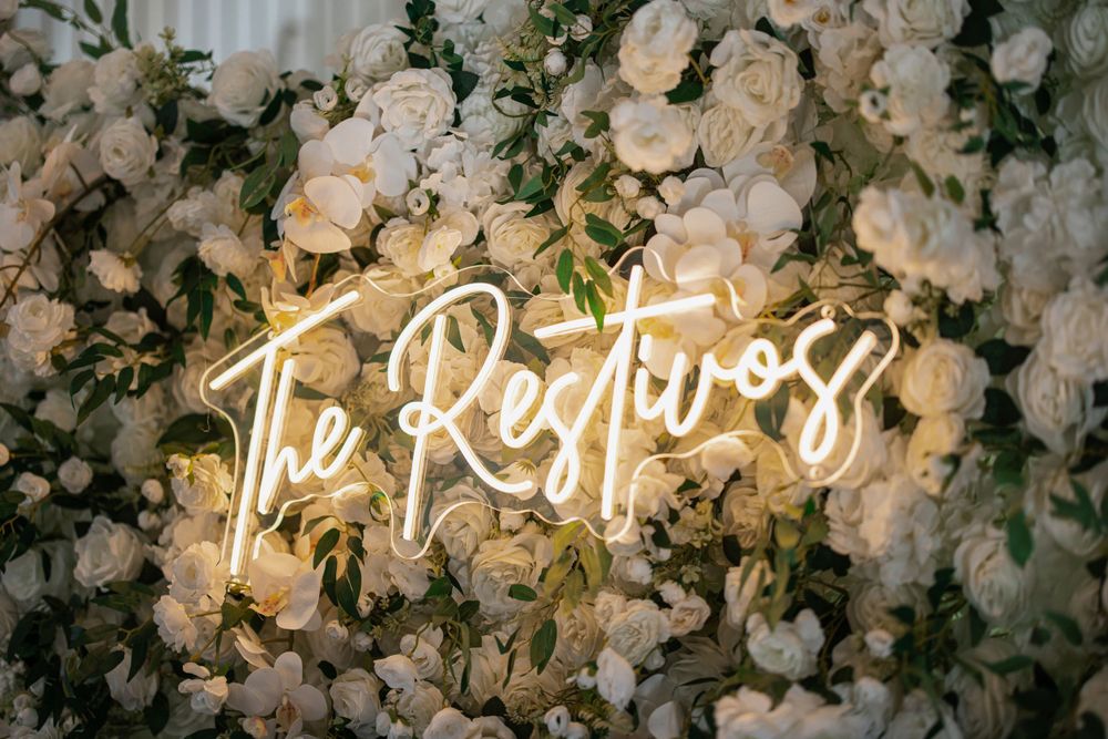 A neon sign reading 'The Restless' glows against a backdrop of white roses.