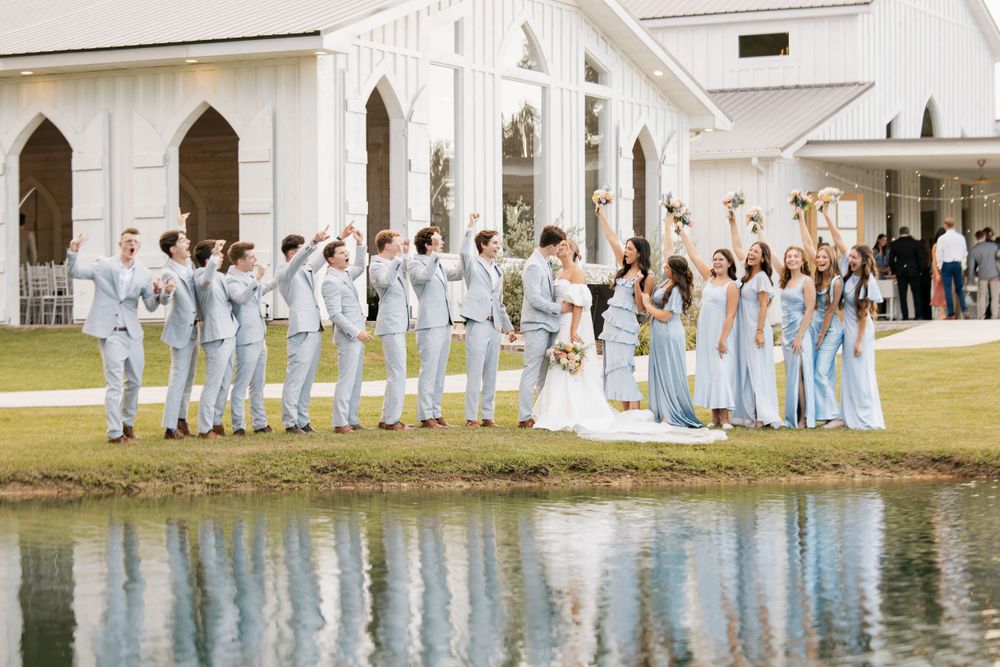 A wedding party in blue and white attire poses along a reflective pond.