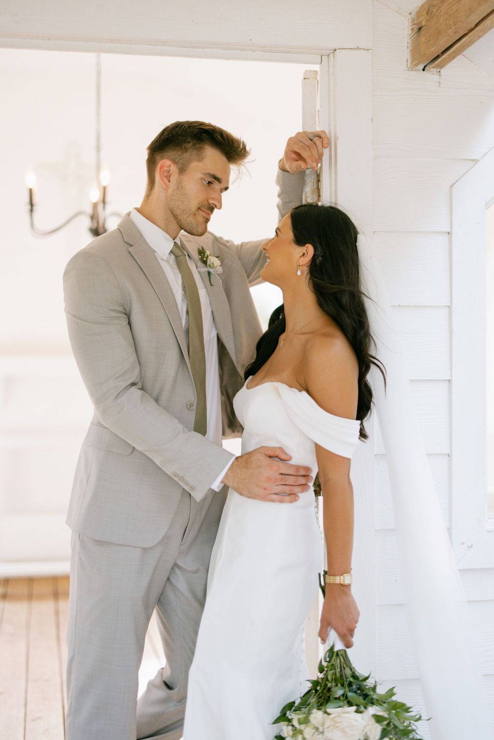 Romantic pose of couple in light gray suit and white dress against bright interior.