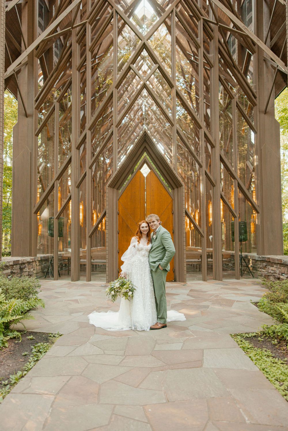 A couple poses for wedding photos in front of an architecturally stunning wooden chapel.