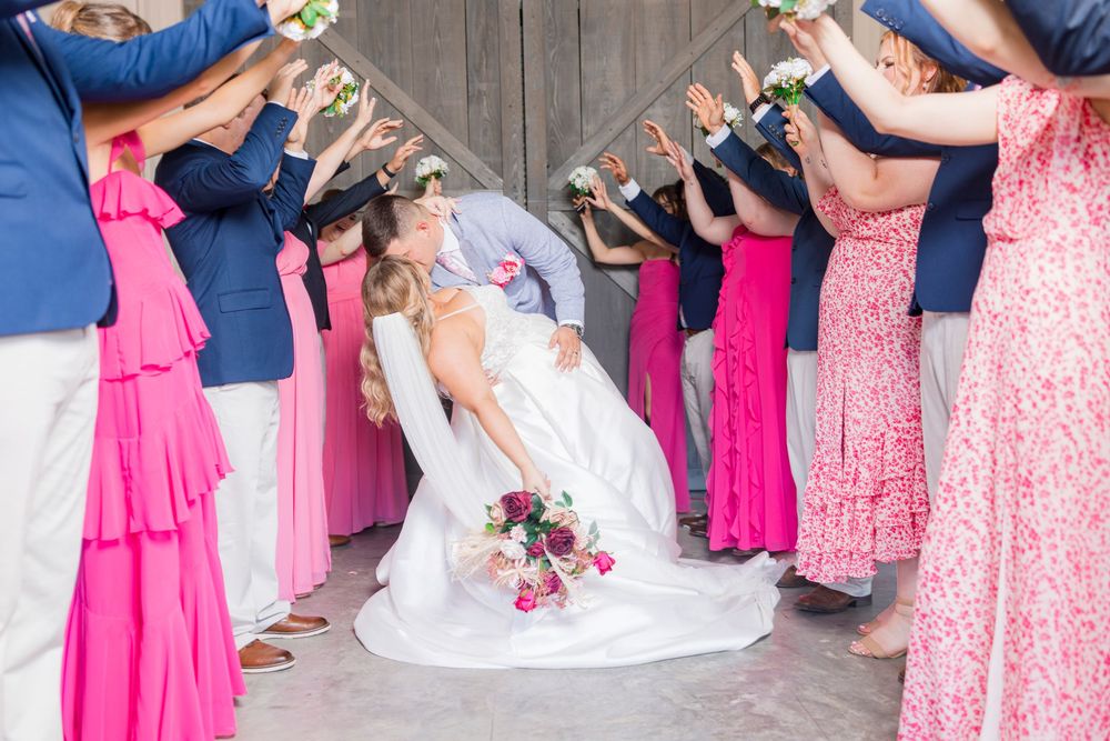 A panoramic wedding party photo showing bridesmaids in pink dresses arranged in a circle with their feet pointed inward.