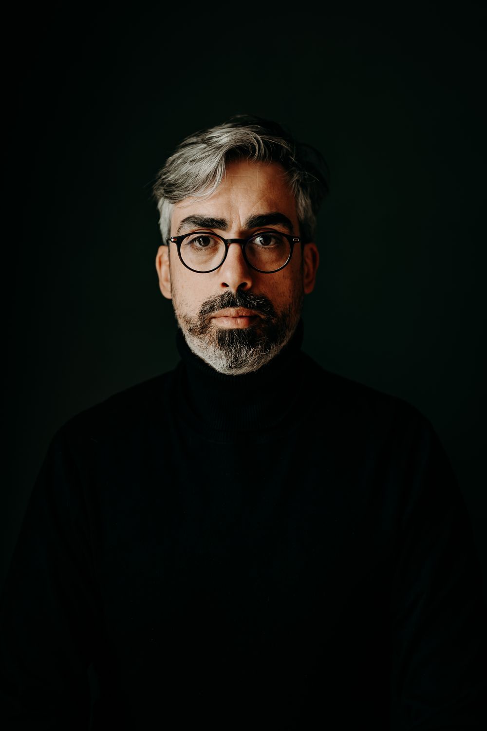 Dramatic low-key portrait series showing a bearded person wearing glasses against dark background.