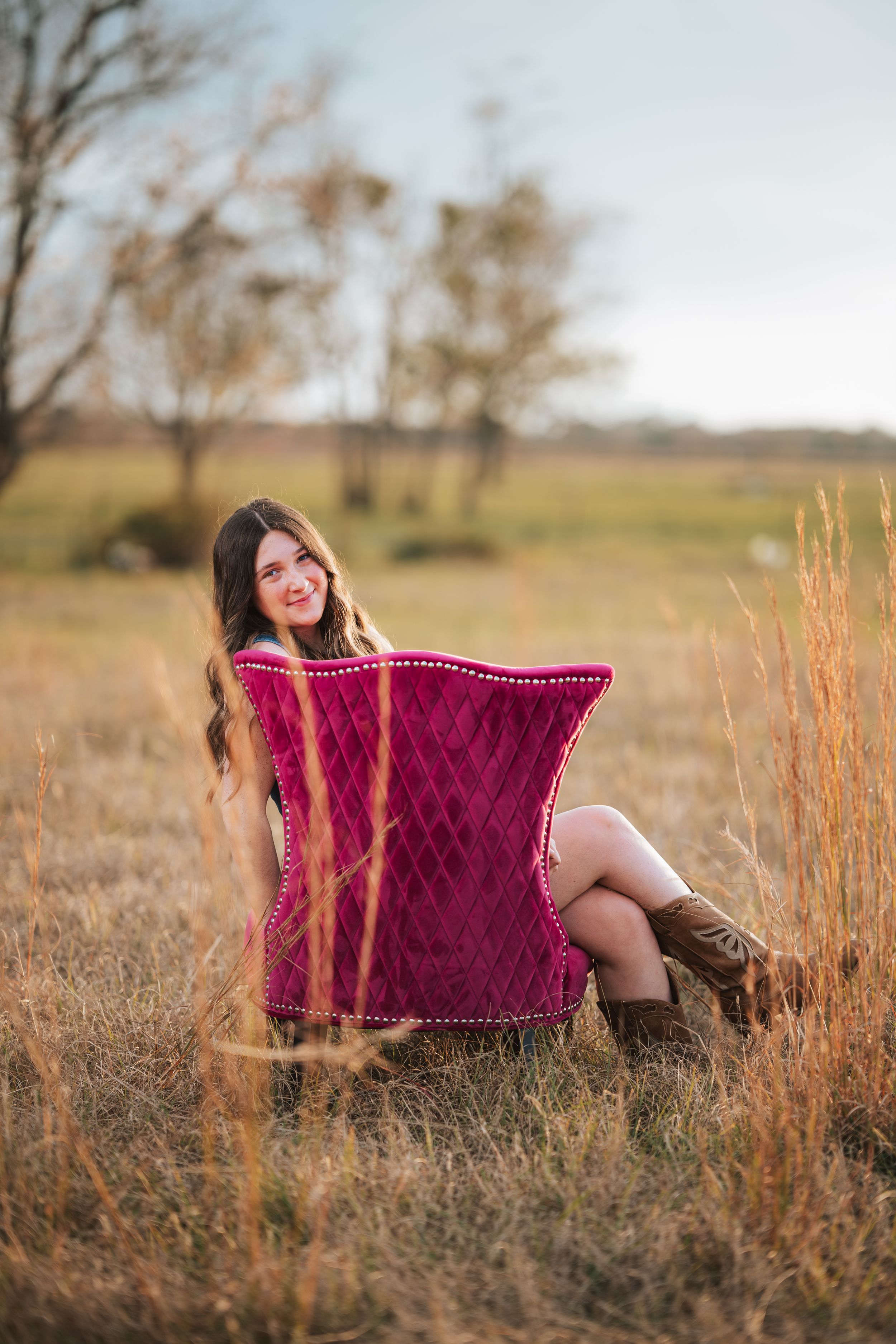 A burgundy velvet chaise lounge sits in a golden field of tall grass during sunset.