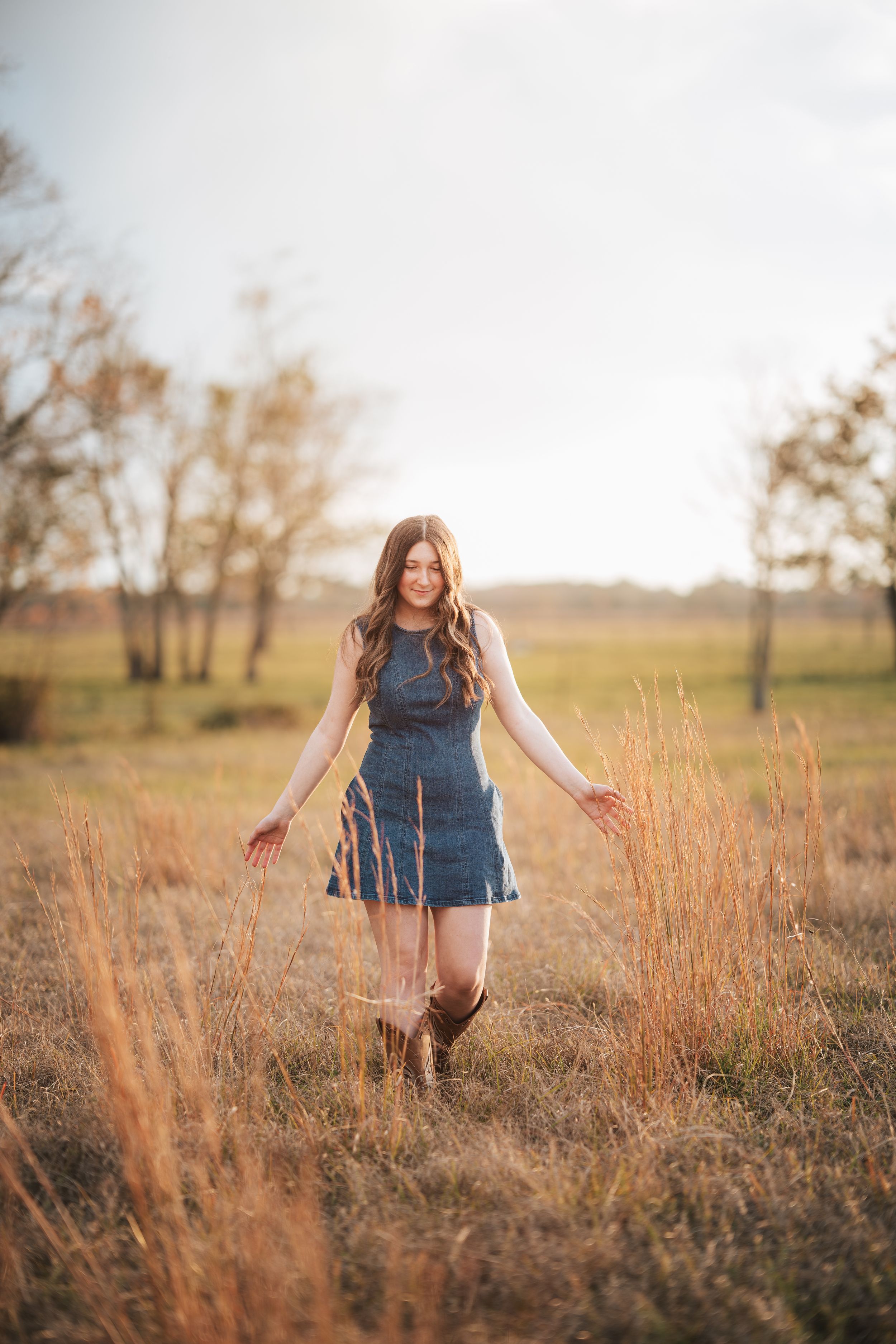 A person in a denim dress walks through a golden field at sunset with warm sunlight creating a dreamy atmosphere.