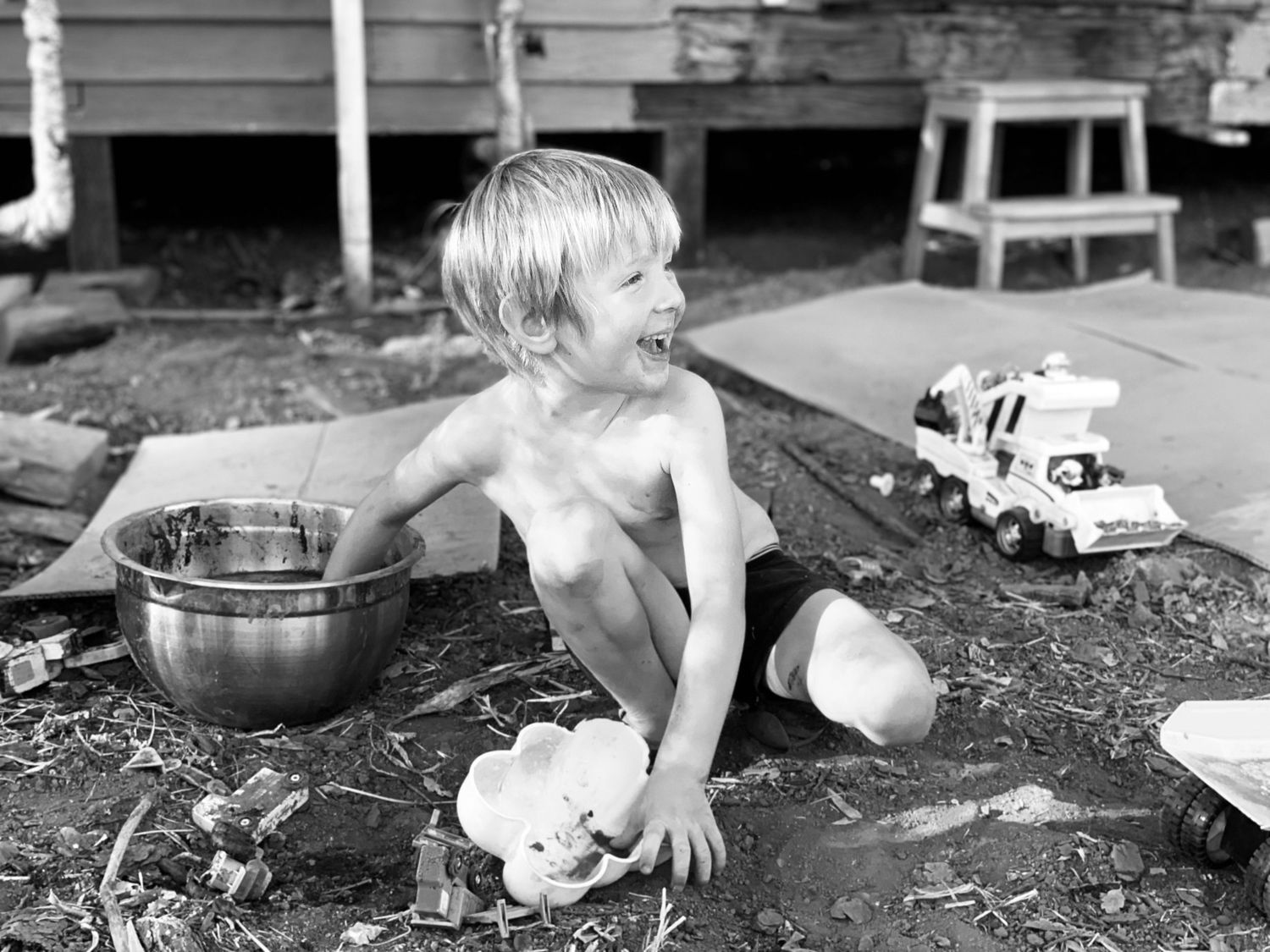 A happy child plays and splashes in the mud outdoors with metal bowls in this vintage black and white photograph.