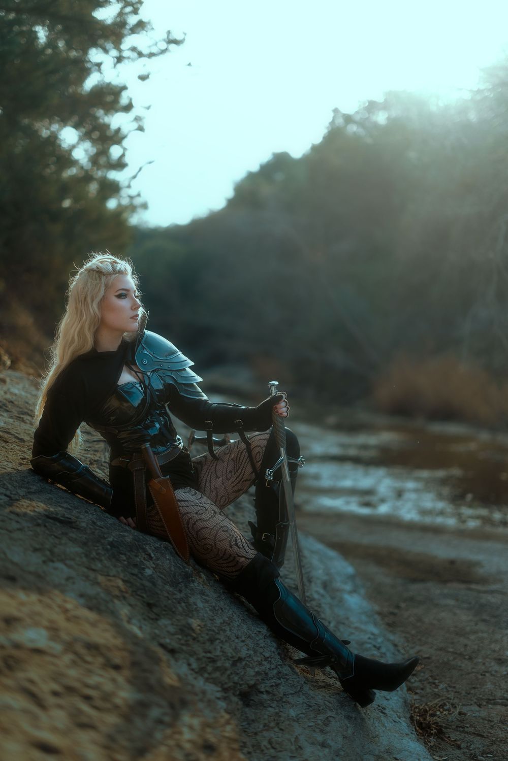 Dramatic cosplay photoshoot by a riverbank in moody lighting.