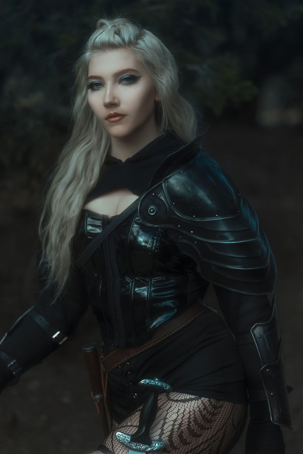 Medieval fantasy costume with black and blue armor in a dark forest setting.
