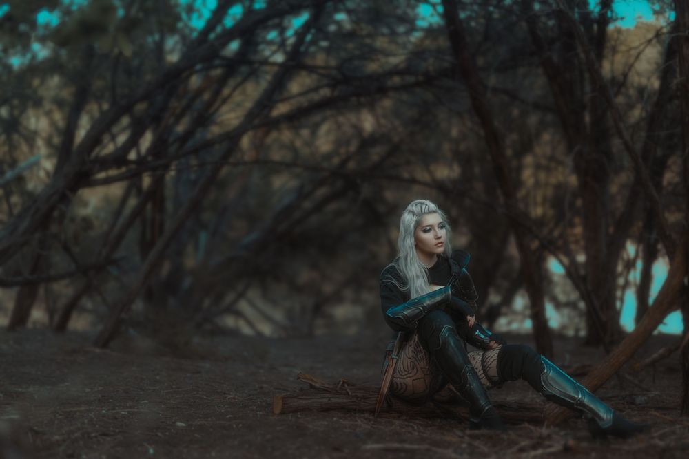 Fantasy-themed photoshoot in a dark forest with turquoise lighting effects.