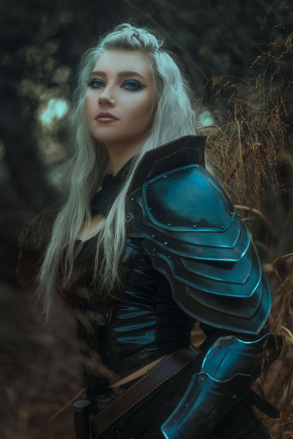 Warrior cosplay featuring metallic blue armor and dramatic forest backdrop.