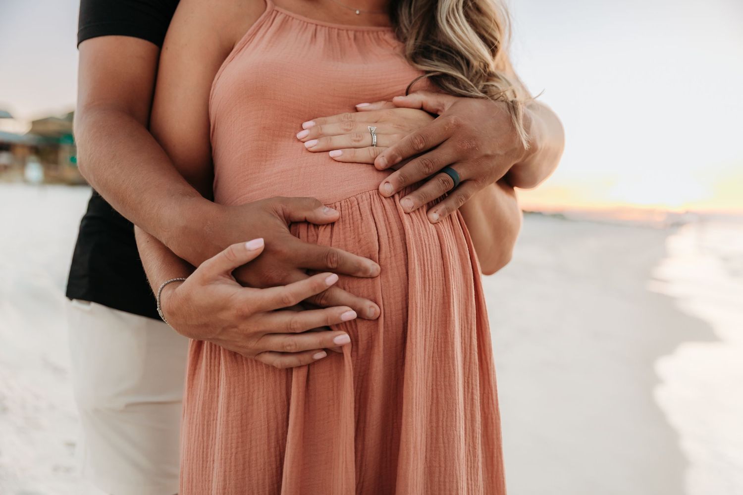 Close-up photos showing hands cradling a pregnant belly in a peach-colored maternity dress against a light background.