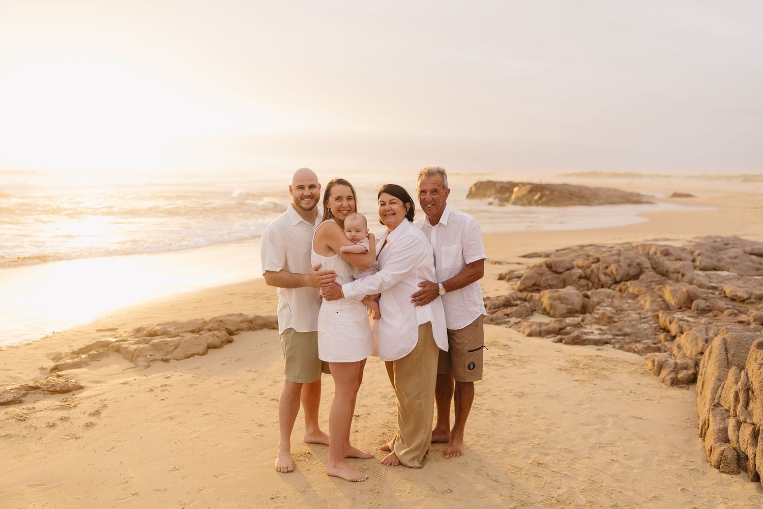 A group stands together on a sandy beach at sunset with coastal cliffs and ocean waves in the background.