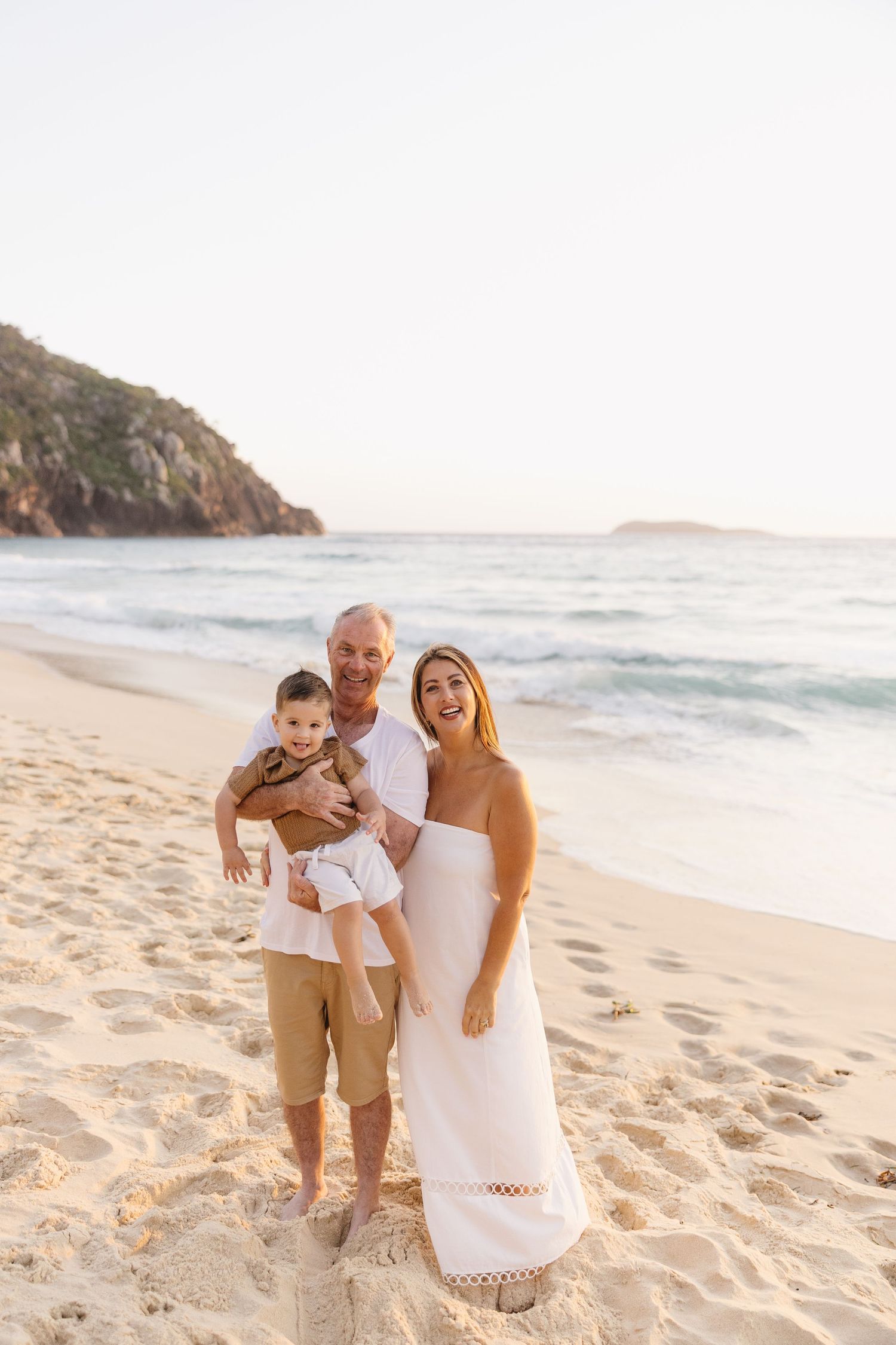 Family enjoying a sunset beach photoshoot with sandy toes and ocean waves in the background.