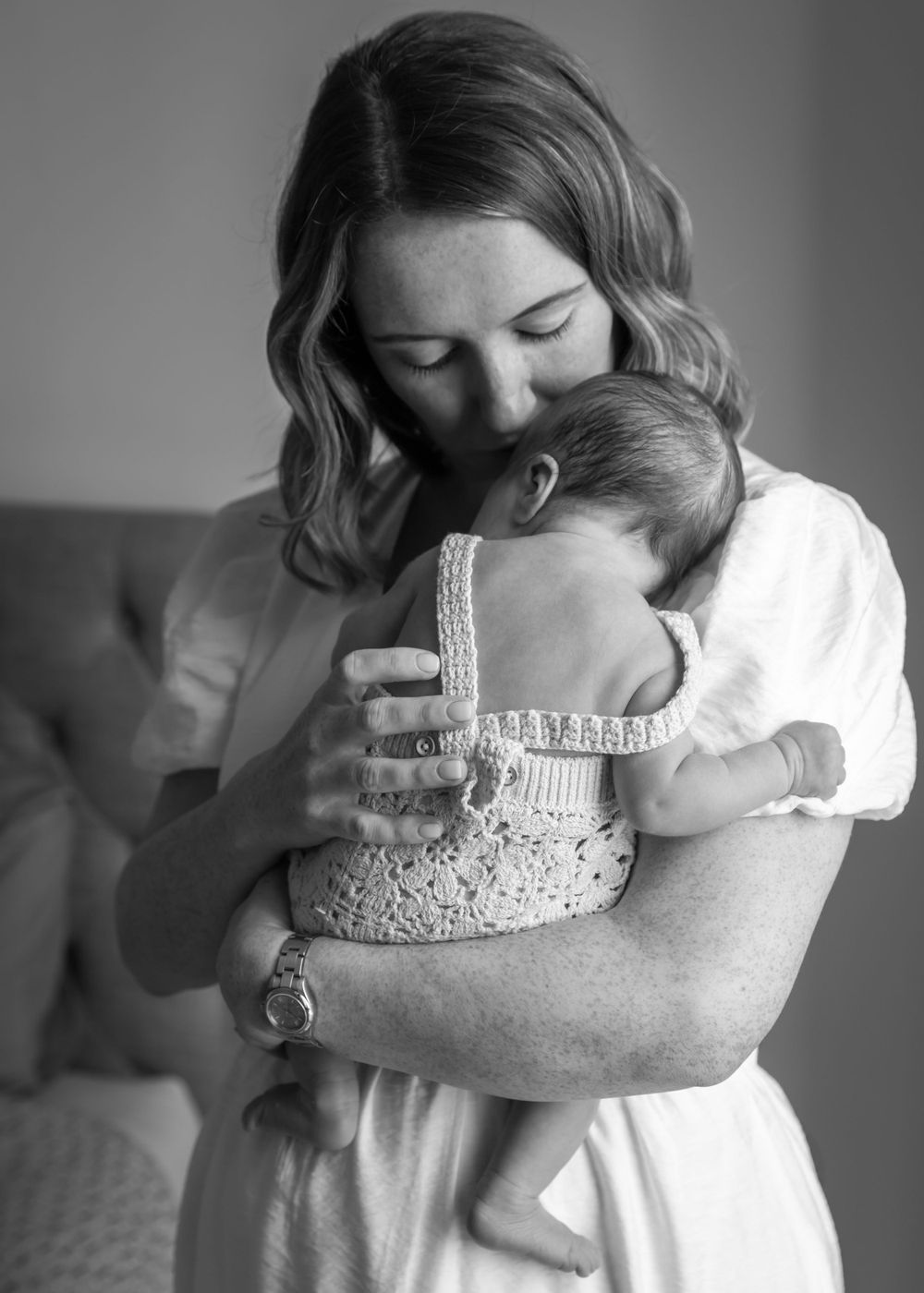 Black and white portrait of a mother holding her newborn baby in a cute little outfit, during at-home newborn photoshoot in Dubai