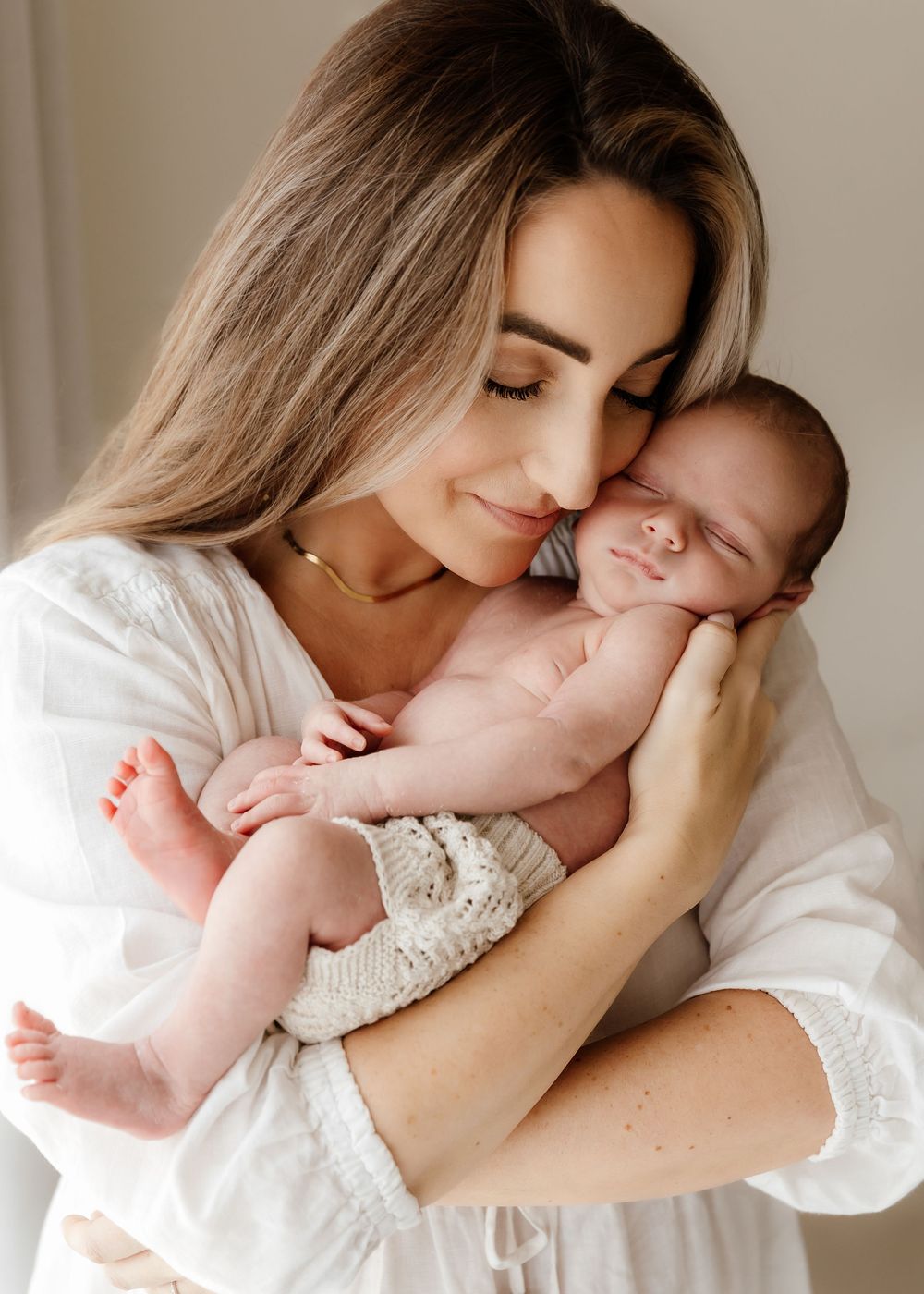 Mother holding her newborn baby cheek to cheek during natural at-home photography session in Dubai