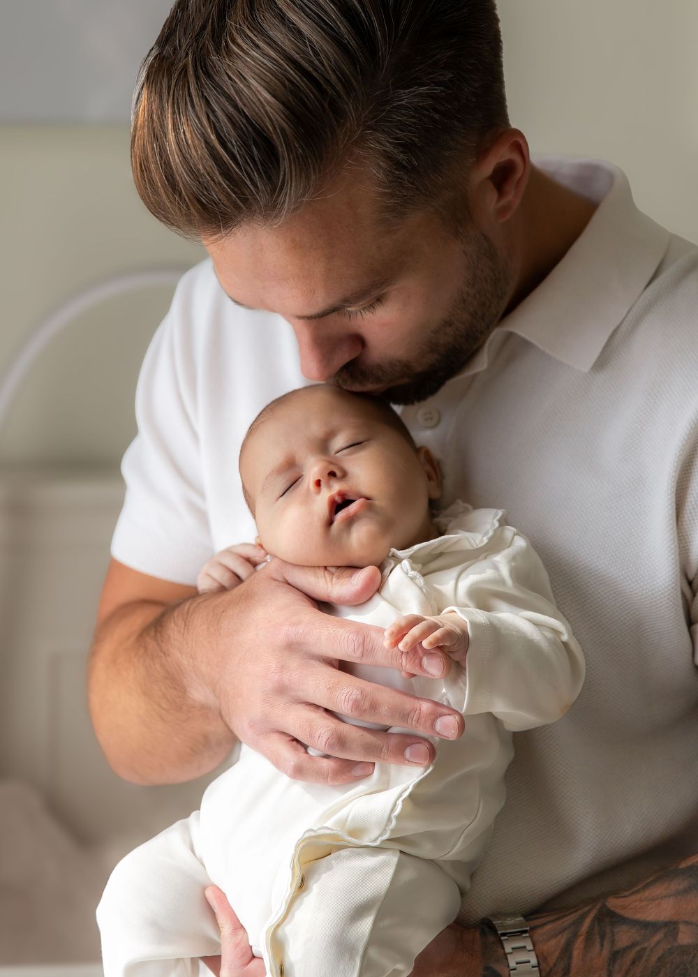 Dad kissing newborn baby on head during natural at-home photography session in Dubai