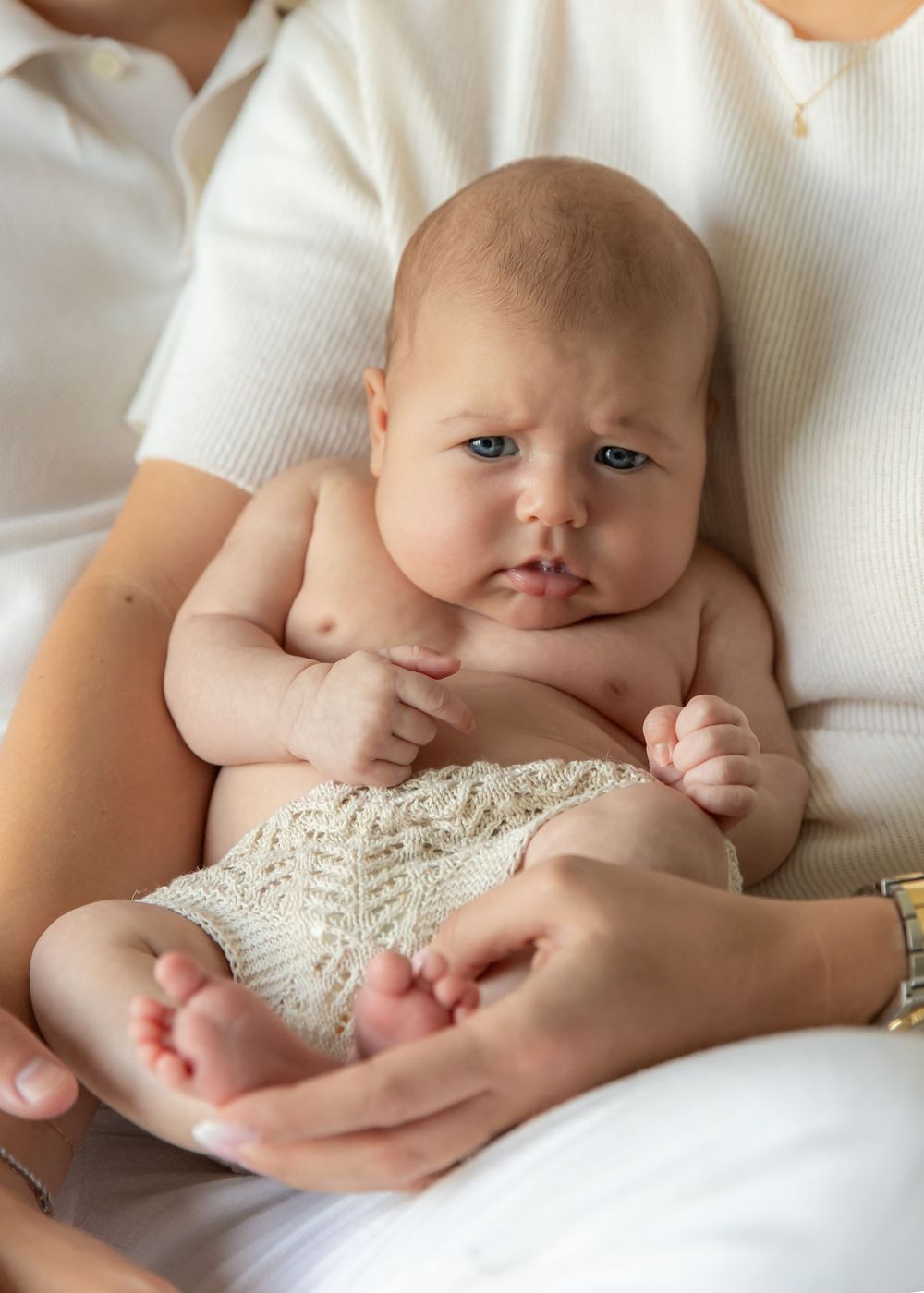 Very cute photo of chubby baby sat on mum's lap at-home during a natural newborn photoshoot in Dubai