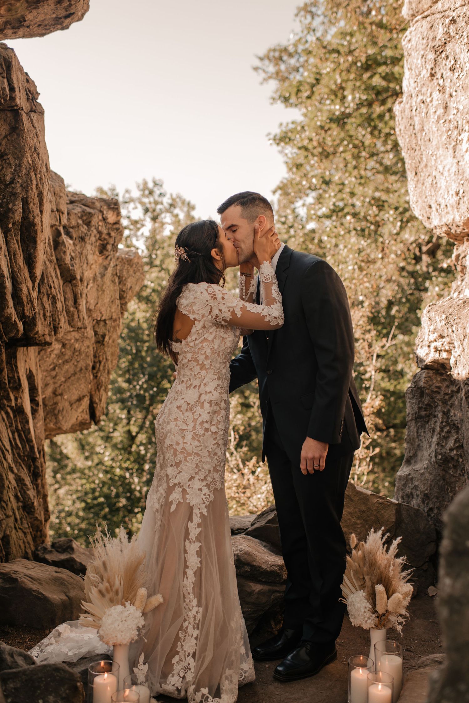 A couple shares an intimate moment among rocky formations decorated with dried florals.