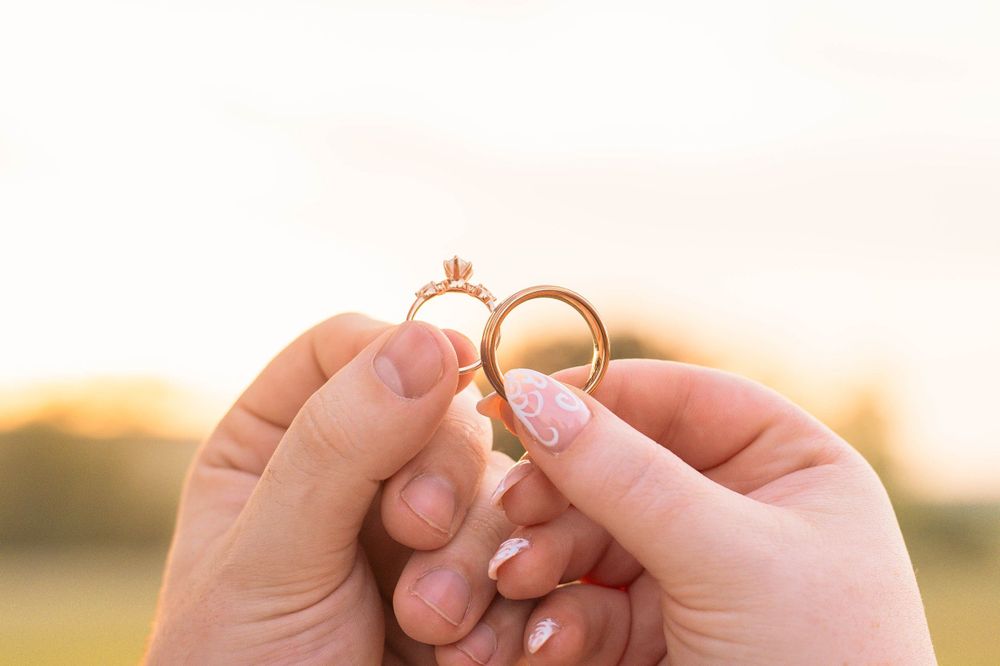 Two hands hold wedding rings against a sunset backdrop.