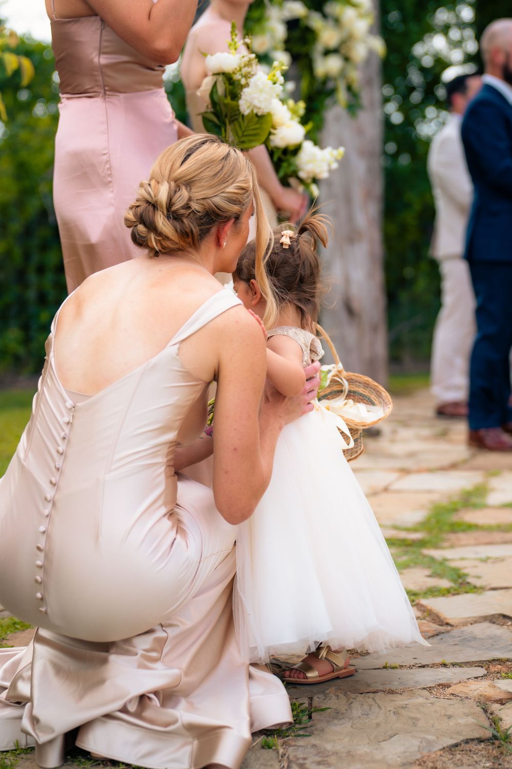 A touching moment between a parent and young child in white dresses at an outdoor wedding ceremony.