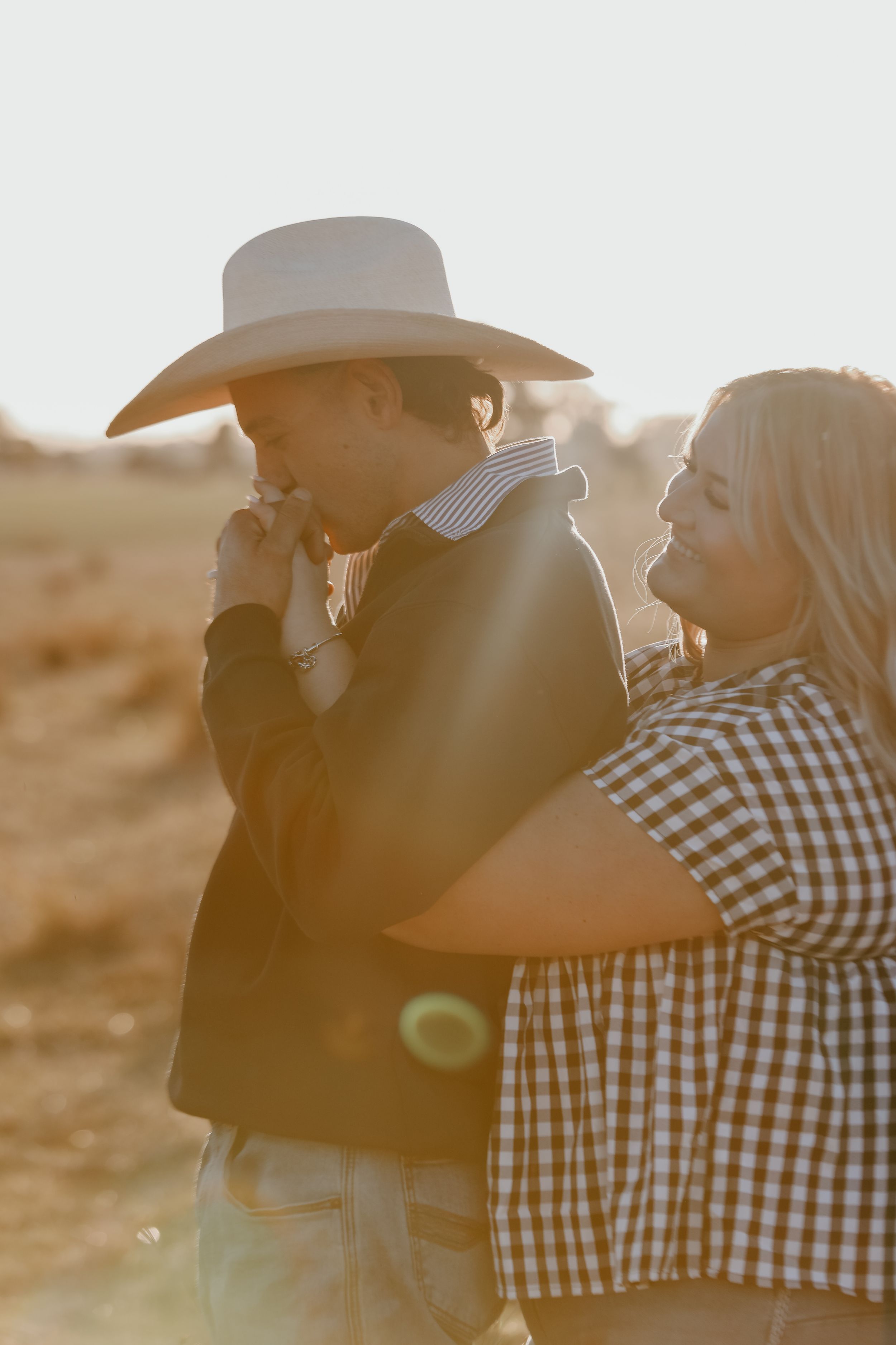 Backlit couple in western wear sharing tender moment during golden hour.