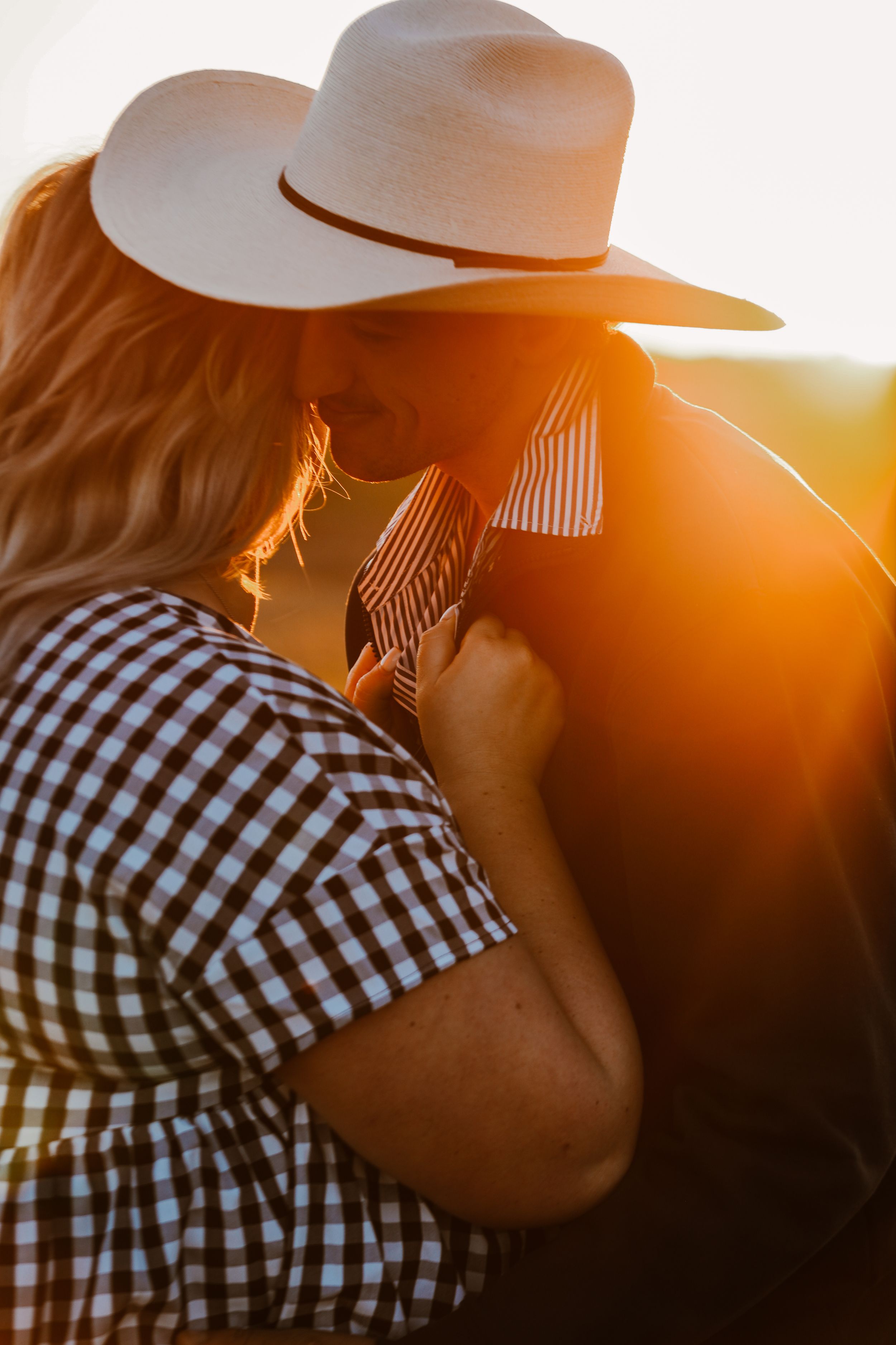 Couple in western attire embracing during golden sunset hour.