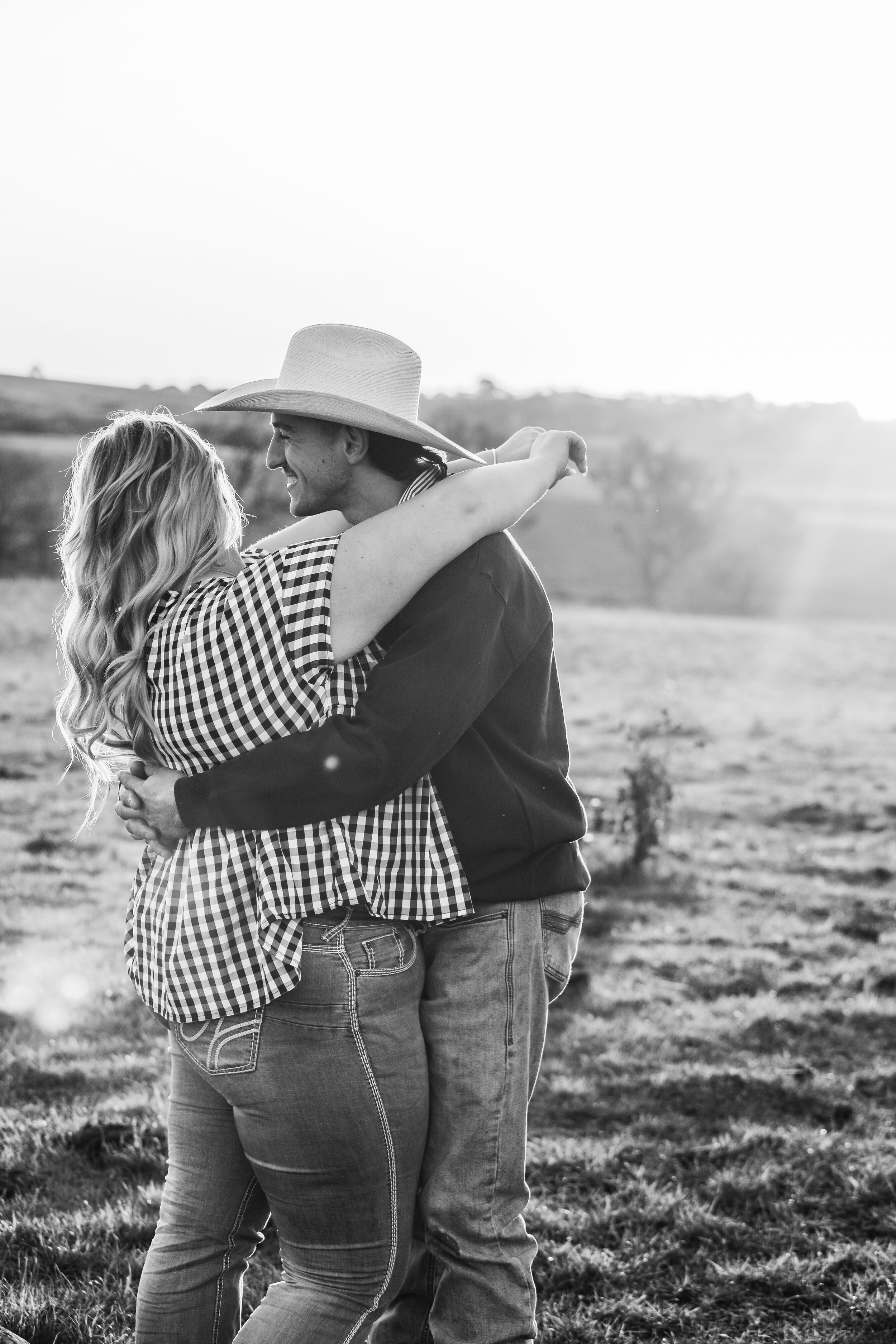 Black and white photo of couple in gingham and jeans embracing on rolling hills.