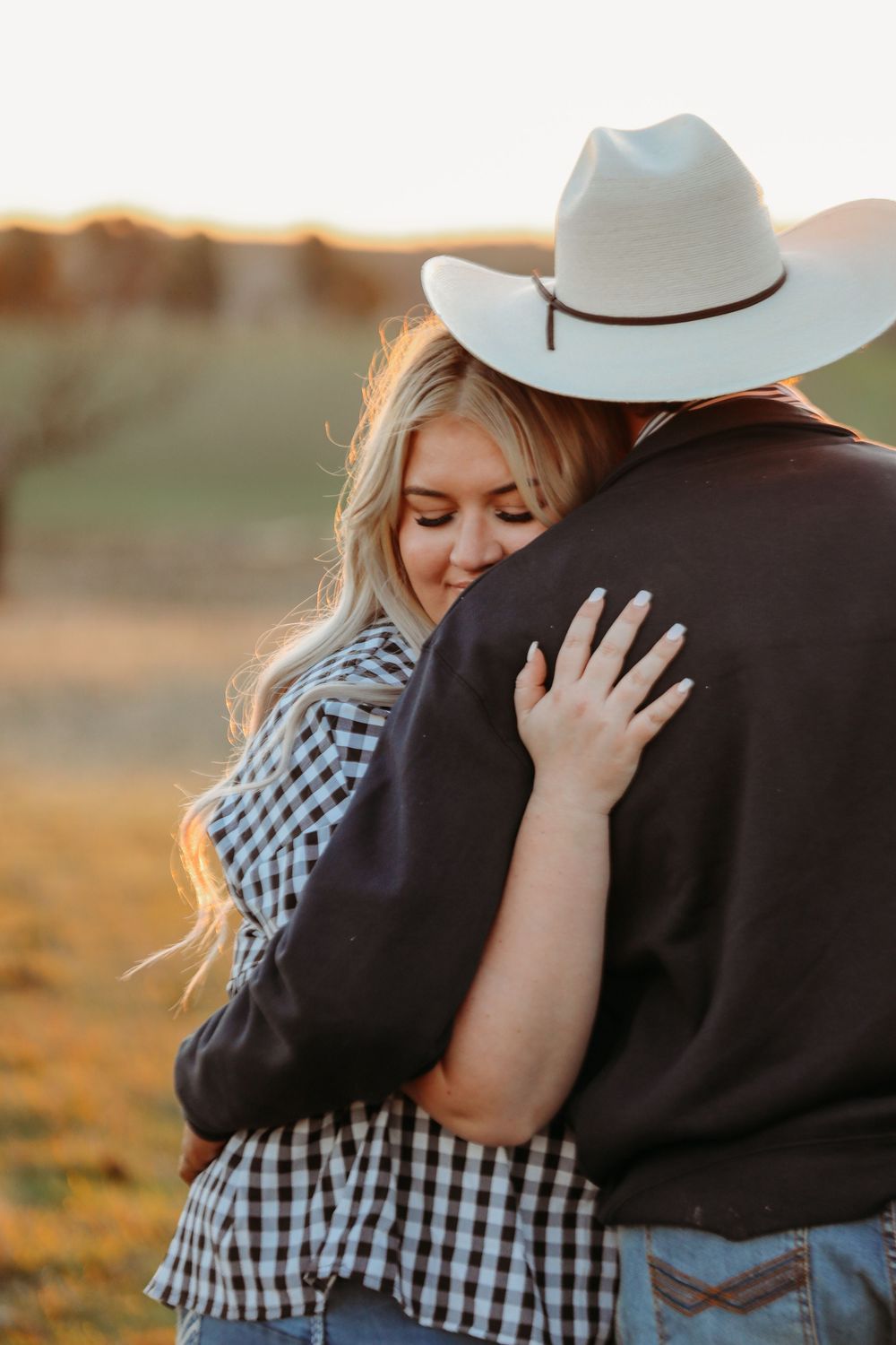 Intimate moment between couple with white cowboy hat against golden sunset.