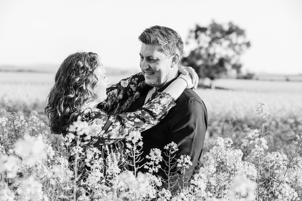 Two people embrace in a blooming canola field at sunset.
