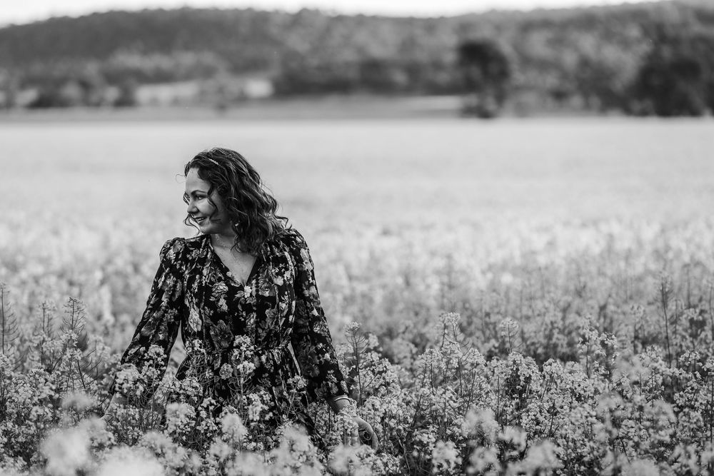 Black and white photo of couple sitting in flowering field with trees on horizon.