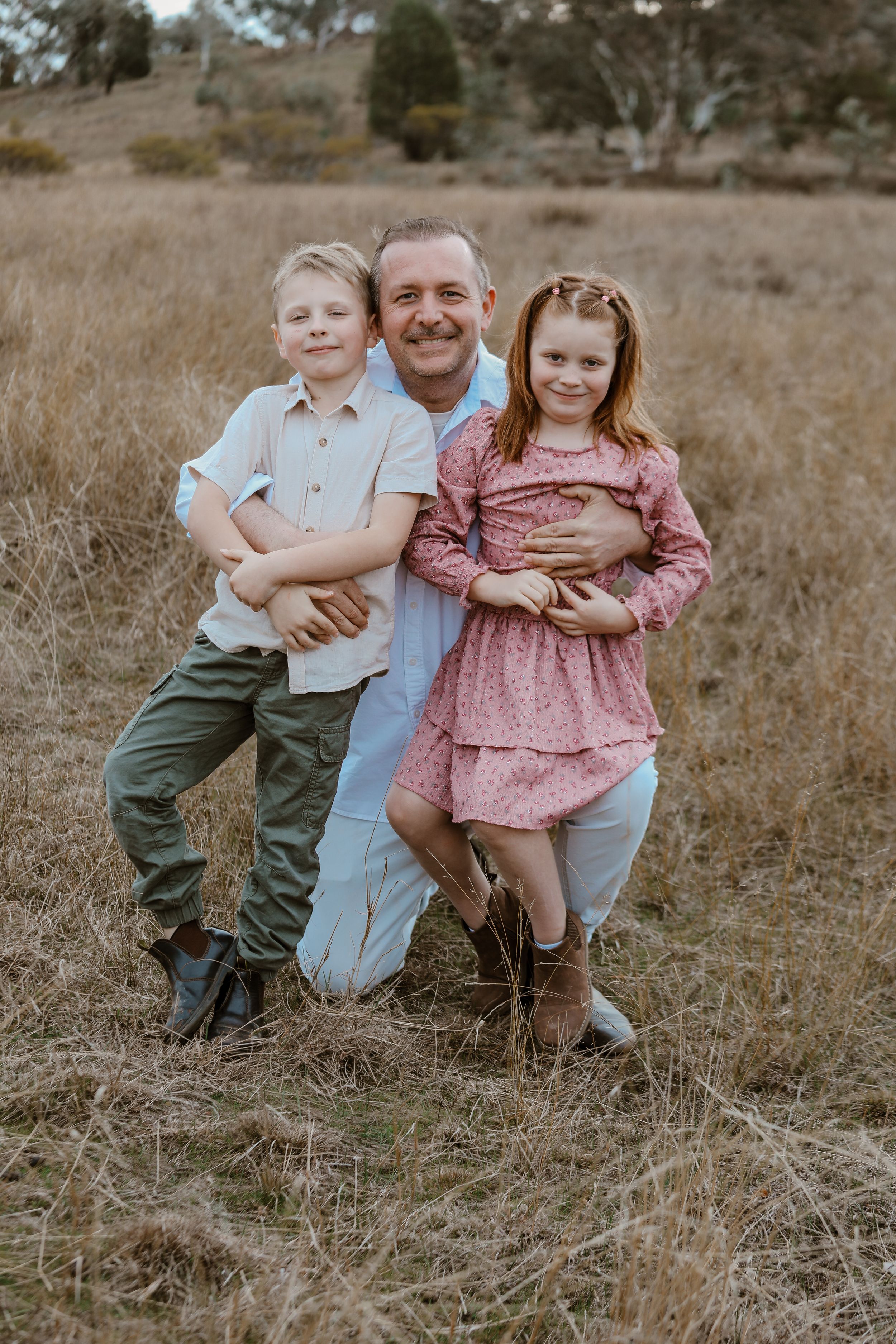 Family sitting together in rustic field setting during sunset photoshoot.