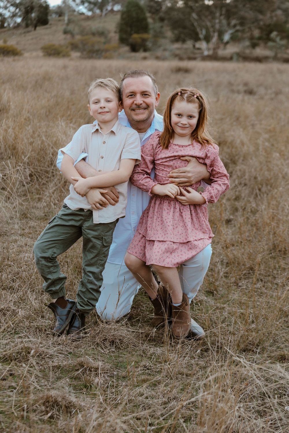 Family sitting together in rustic field setting during sunset photoshoot.